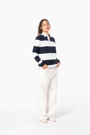 Jeune femme bouclée cheveux attachés qui porte un polo de rugby rayé blanc et bleu marine.