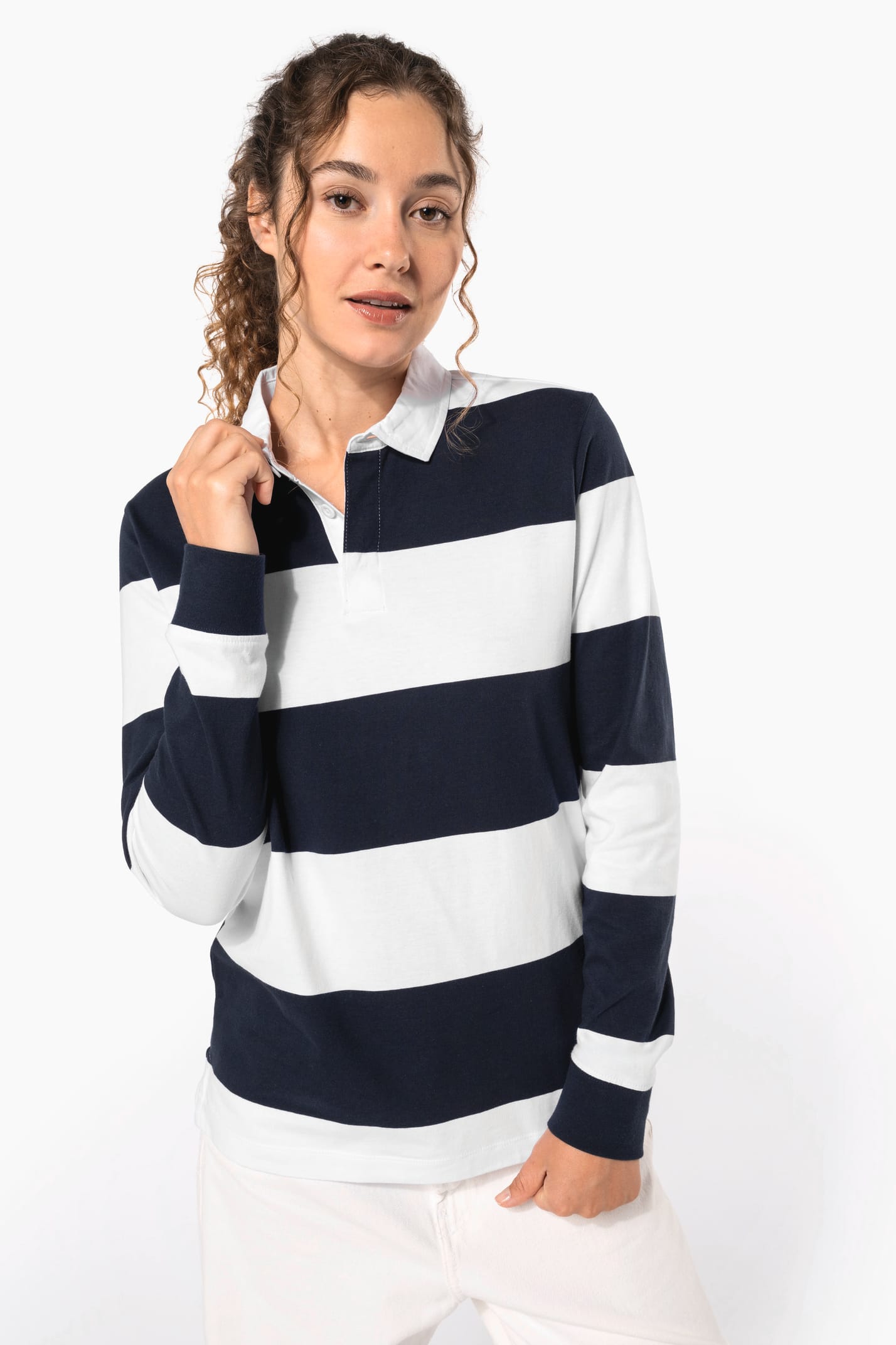 Jeune femme bouclée cheveux attachés qui porte un polo de rugby rayé blanc et bleu marine.