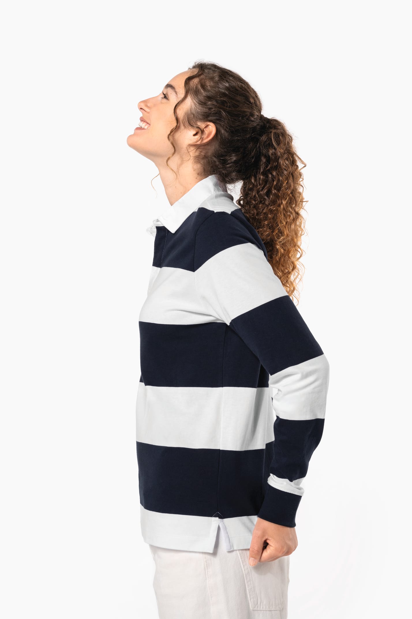 Jeune femme bouclée cheveux attachés qui porte un polo de rugby rayé blanc et bleu marine.