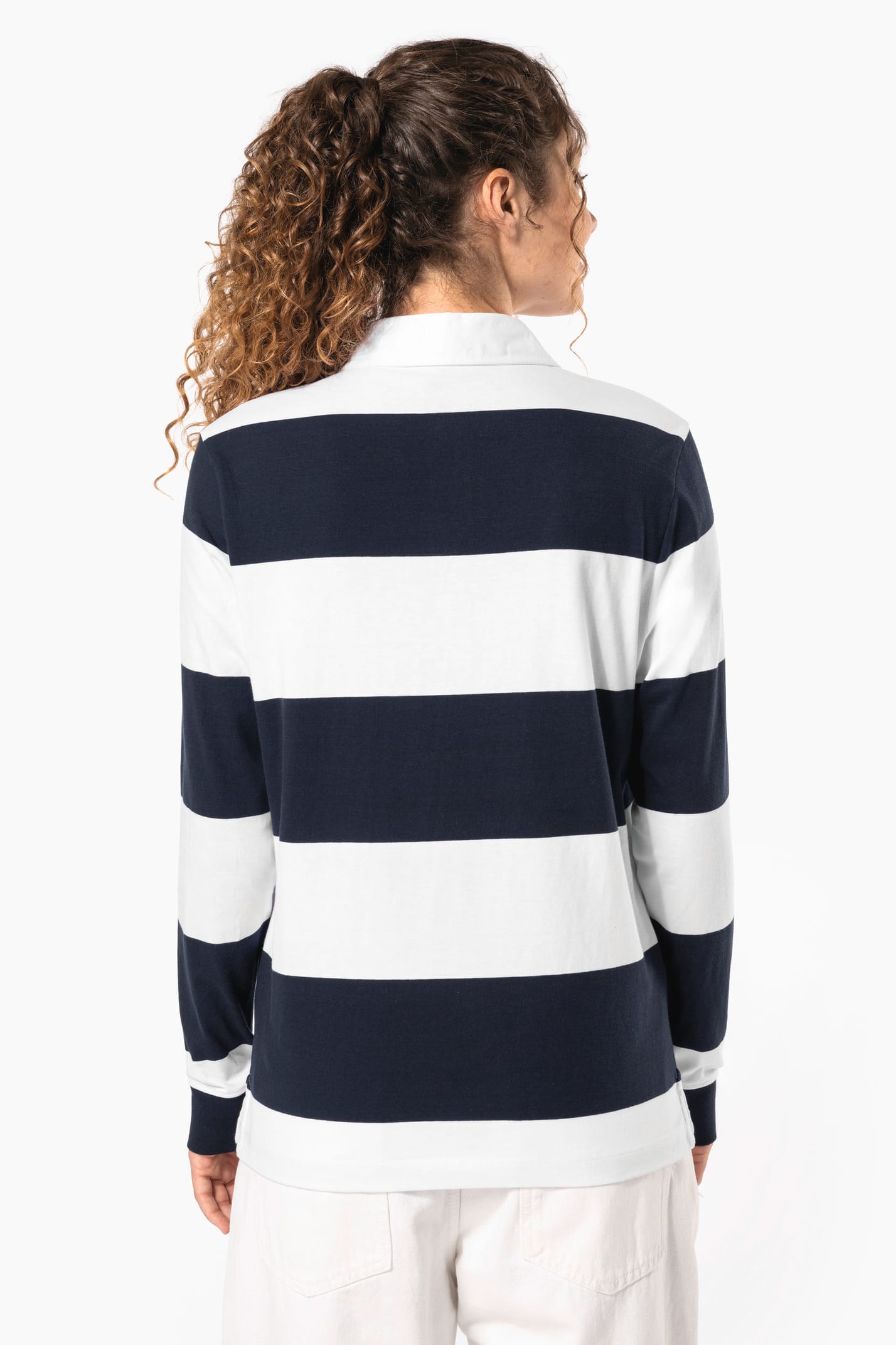 Jeune femme bouclée cheveux attachés qui porte un polo de rugby rayé blanc et bleu marine.