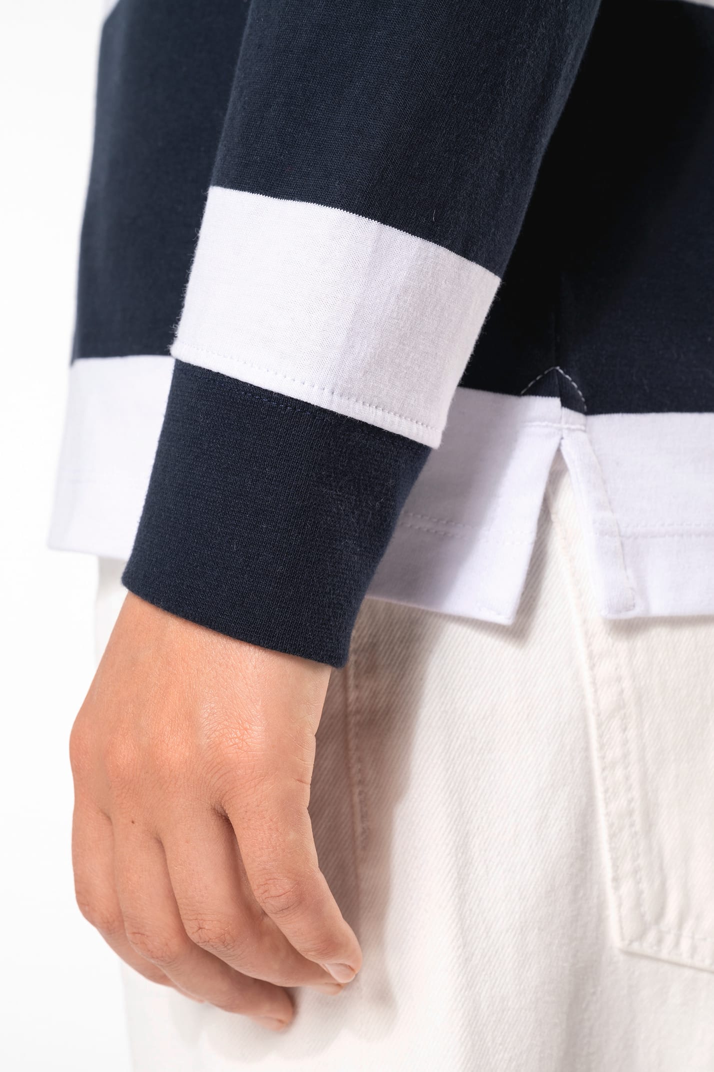 Jeune femme bouclée cheveux attachés qui porte un polo de rugby rayé blanc et bleu marine.