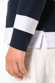 Jeune femme bouclée cheveux attachés qui porte un polo de rugby rayé blanc et bleu marine.