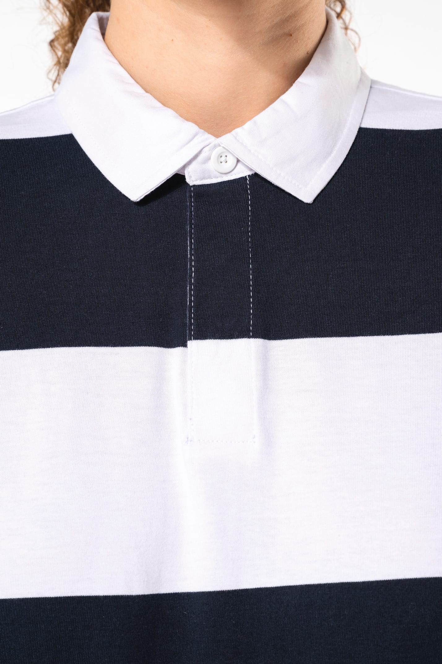 Jeune femme bouclée cheveux attachés qui porte un polo de rugby rayé blanc et bleu marine.