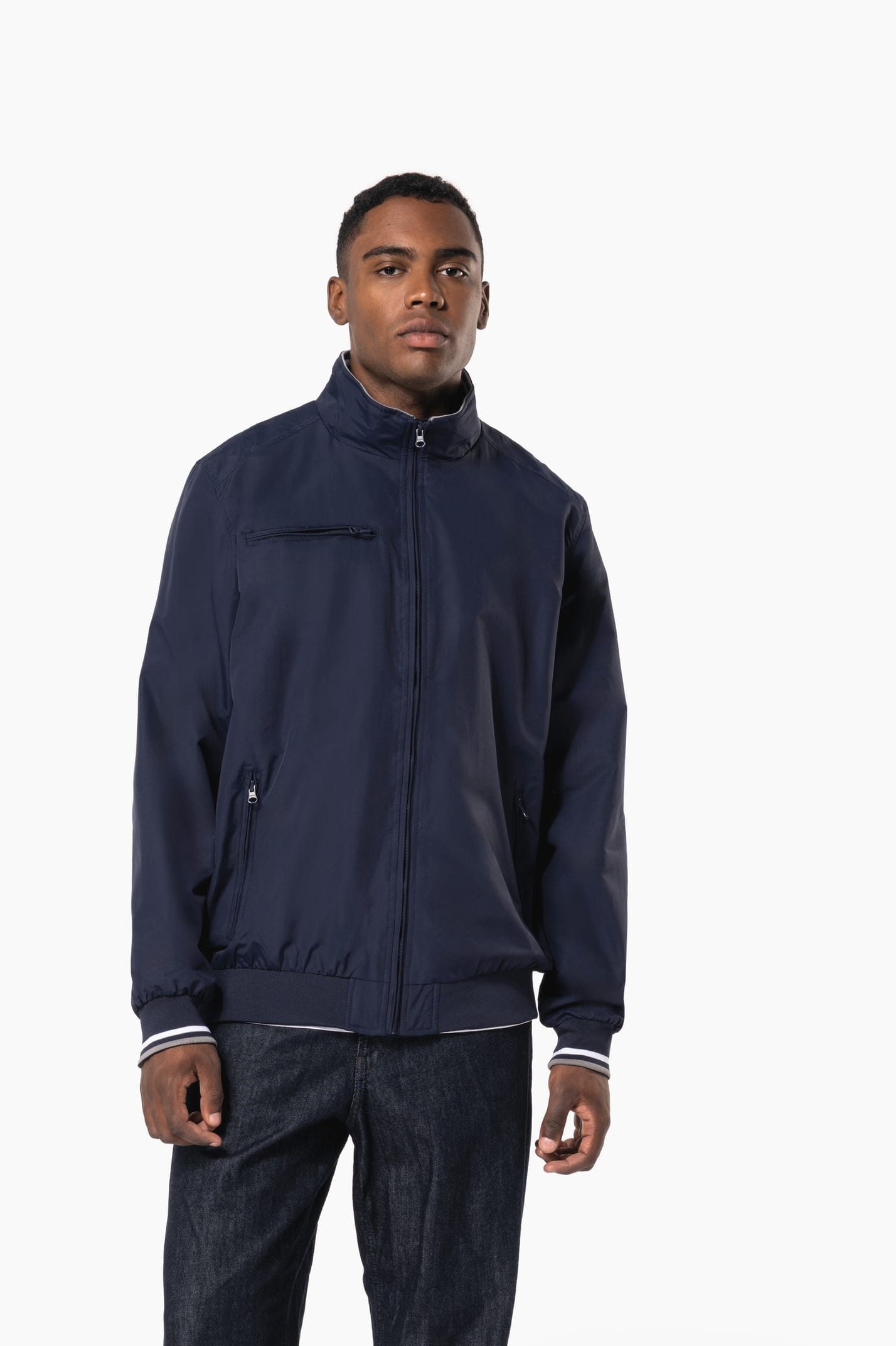 Homme brun cheveux courts qui porte un blouson style bomber américain bleu marine.