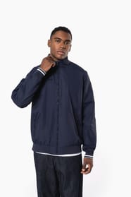 Homme brun cheveux courts qui porte un blouson style bomber américain bleu marine.
