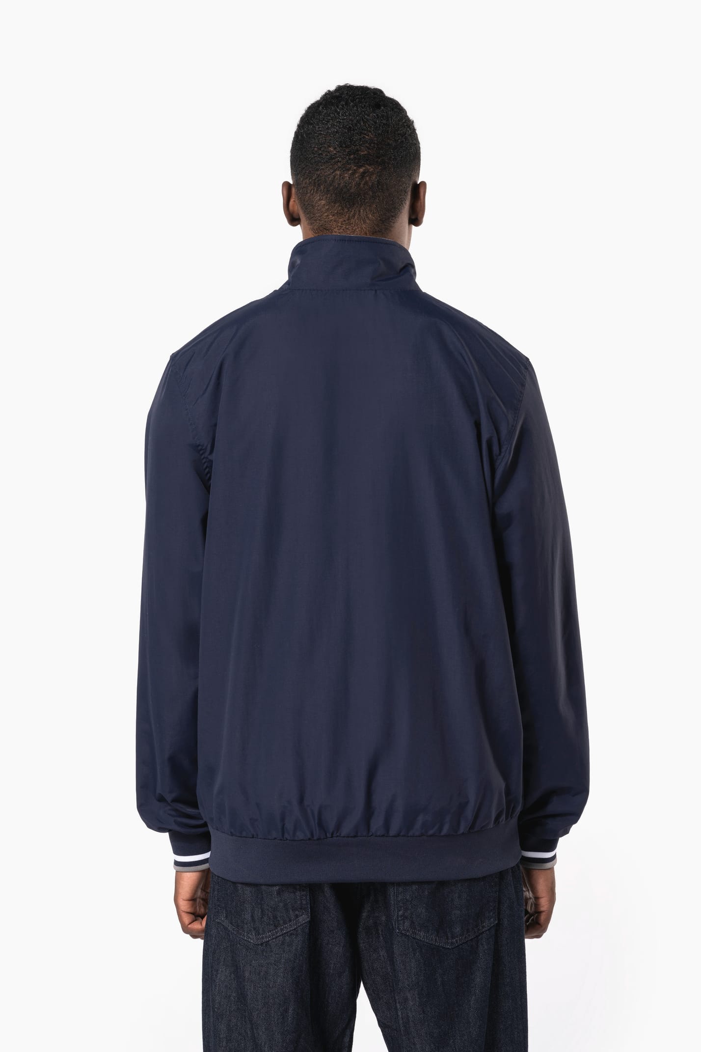 Homme brun cheveux courts qui porte un blouson style bomber américain bleu marine.