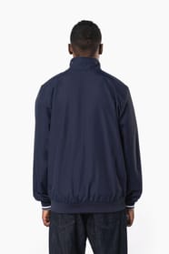 Homme brun cheveux courts qui porte un blouson style bomber américain bleu marine.