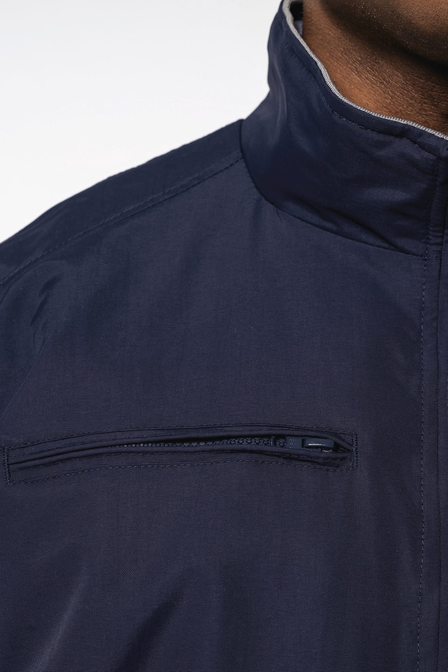 Homme brun cheveux courts qui porte un blouson style bomber américain bleu marine.