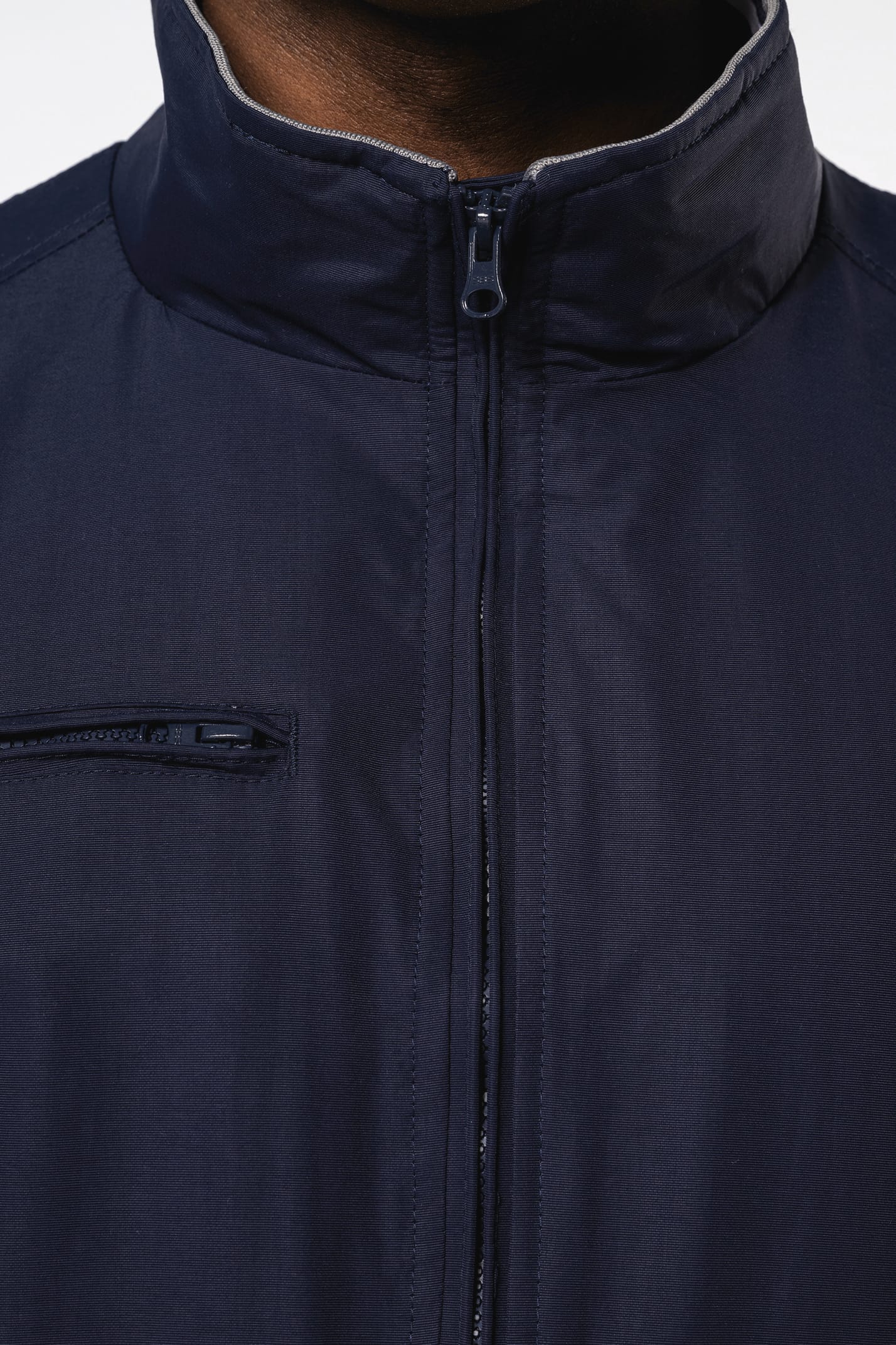 Homme brun cheveux courts qui porte un blouson style bomber américain bleu marine.