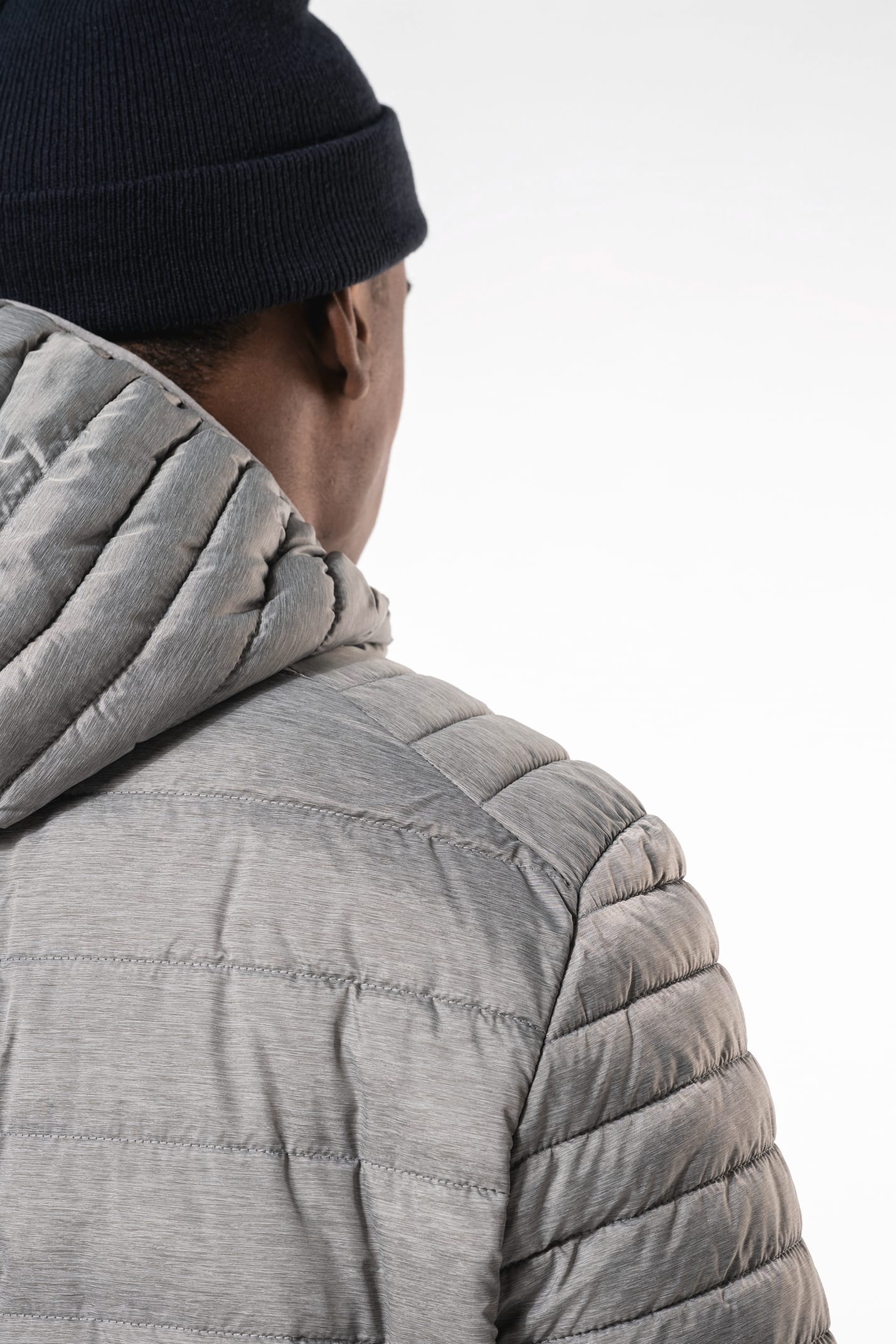 Homme brun avec un bonnet noir qui porte une doudoune légère à capuche argentée.