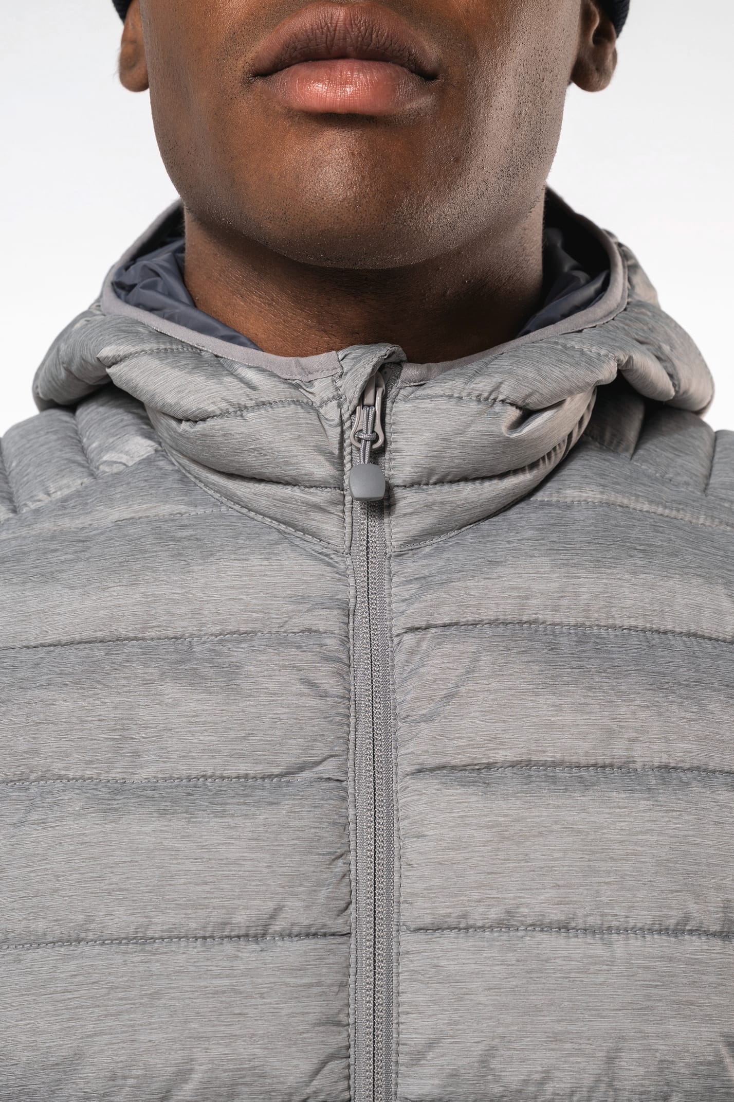 Homme brun avec un bonnet noir qui porte une doudoune légère à capuche argentée.