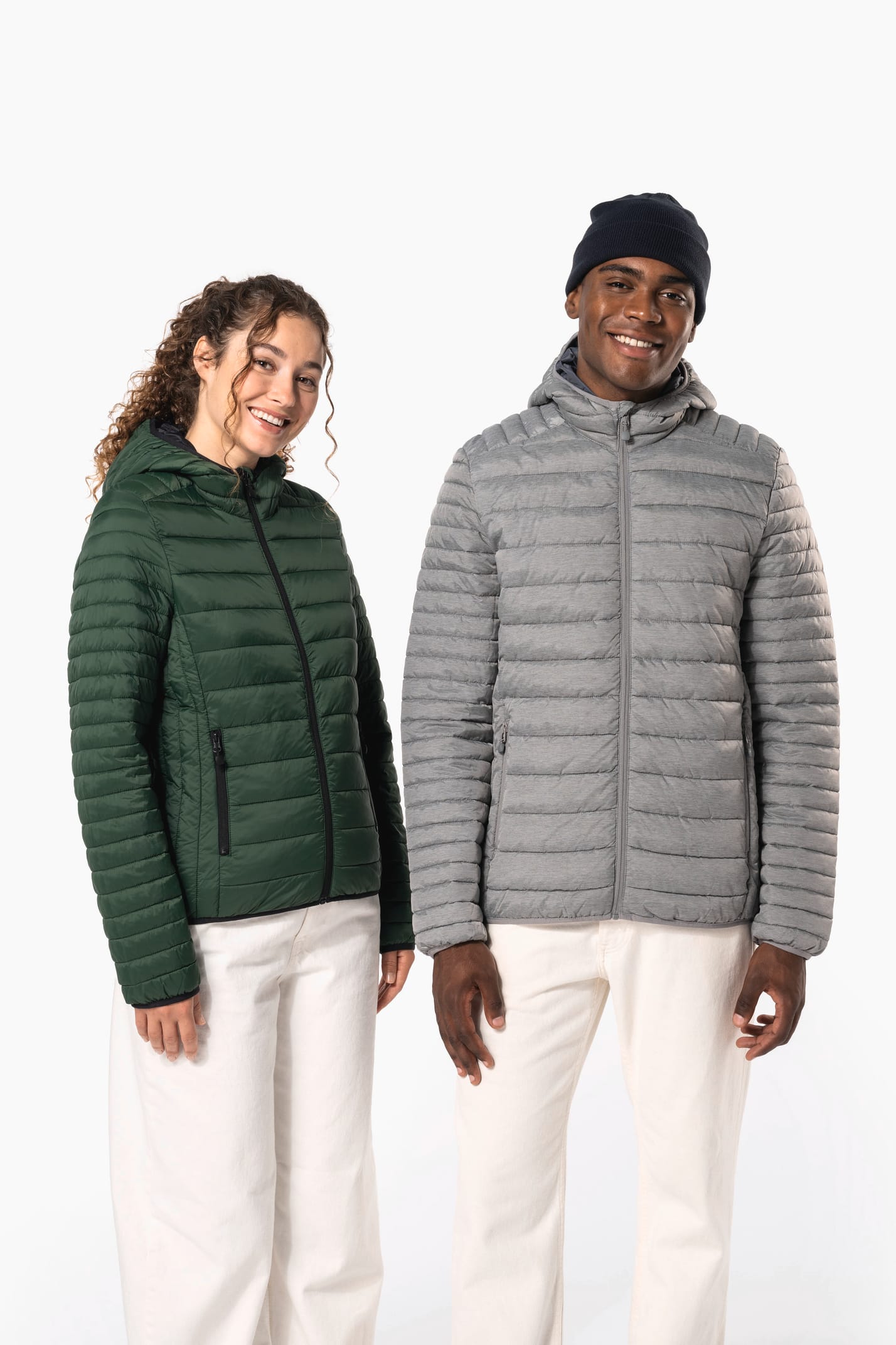Femme aux cheveux frisls attachés et homme brun avec bonnet noir qui portent des doudounes légères à capuches vert forêt et argenté.
