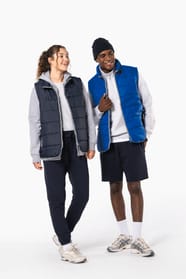 Jeune femme cheveux frisés attachés et  homme avec bonnet noir qui portent des bodywarmers matelassés bleu marine et bleu clair.