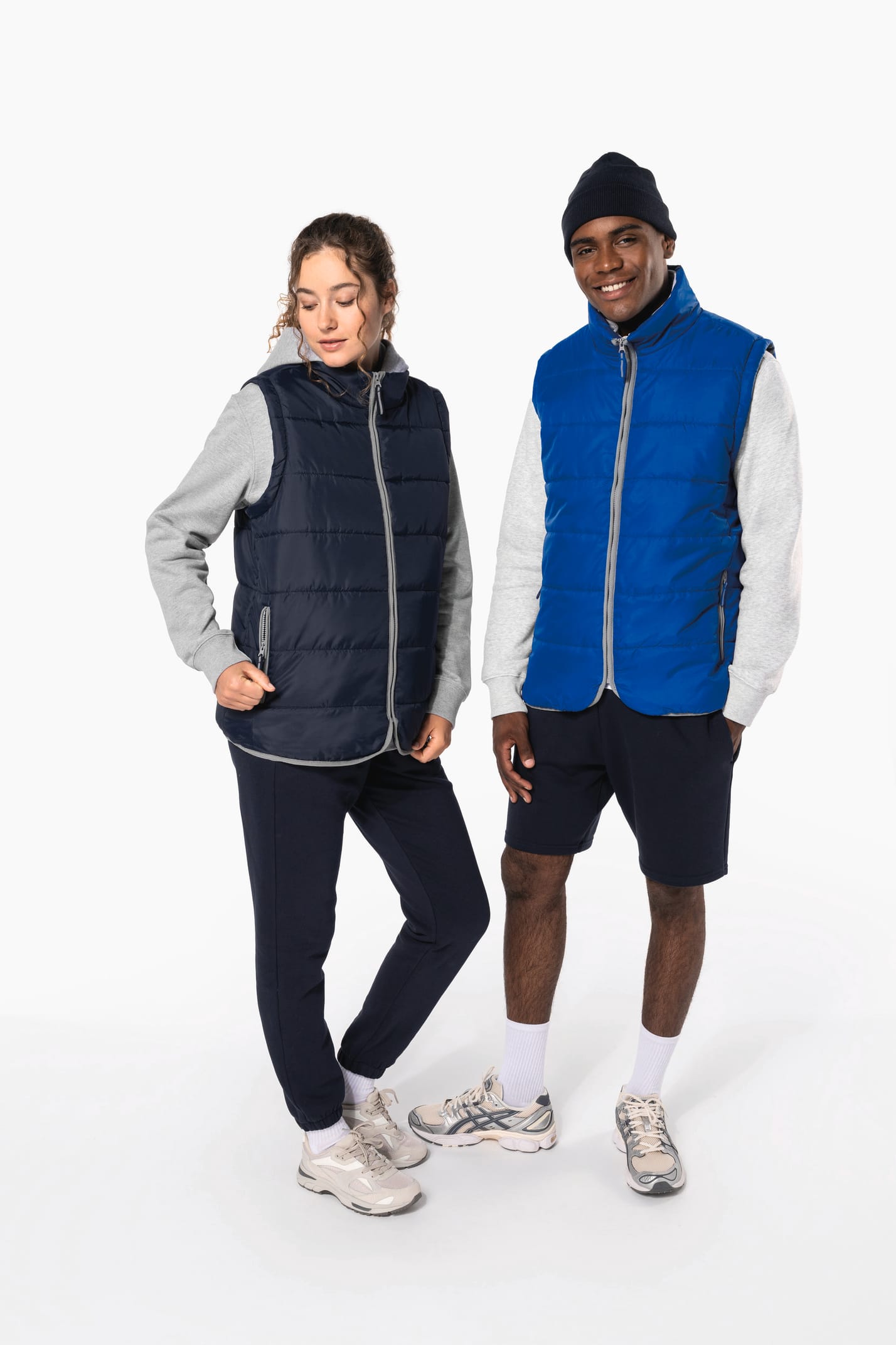 Jeune femme cheveux frisés attachés et  homme avec bonnet noir qui portent des bodywarmers matelassés bleu marine et bleu clair.