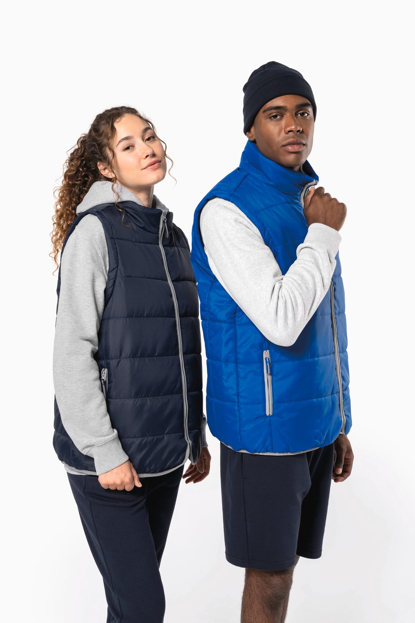 Jeune femme cheveux frisés attachés et  homme avec bonnet noir qui portent des bodywarmers matelassés bleu marine et bleu clair.