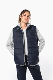 Jeune femme cheveux frisés attachés qui porte un bodywarmer matelassé bleu marine.