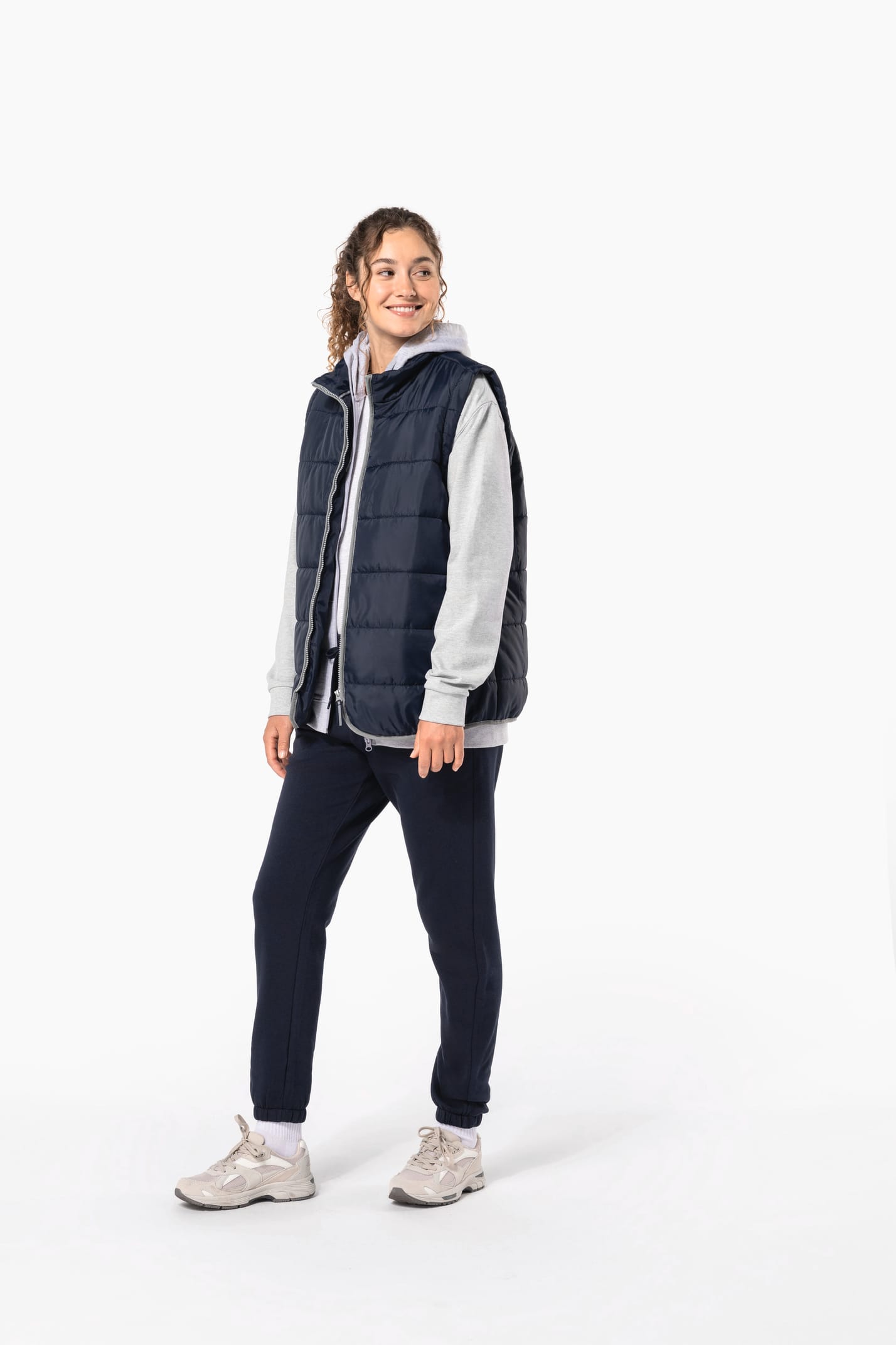 Jeune femme cheveux frisés attachés qui porte un bodywarmer matelassé bleu marine.