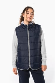 Jeune femme cheveux frisés attachés qui porte un bodywarmer matelassé bleu marine.