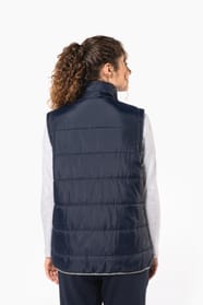 Jeune femme cheveux frisés attachés qui porte un bodywarmer matelassé bleu marine.