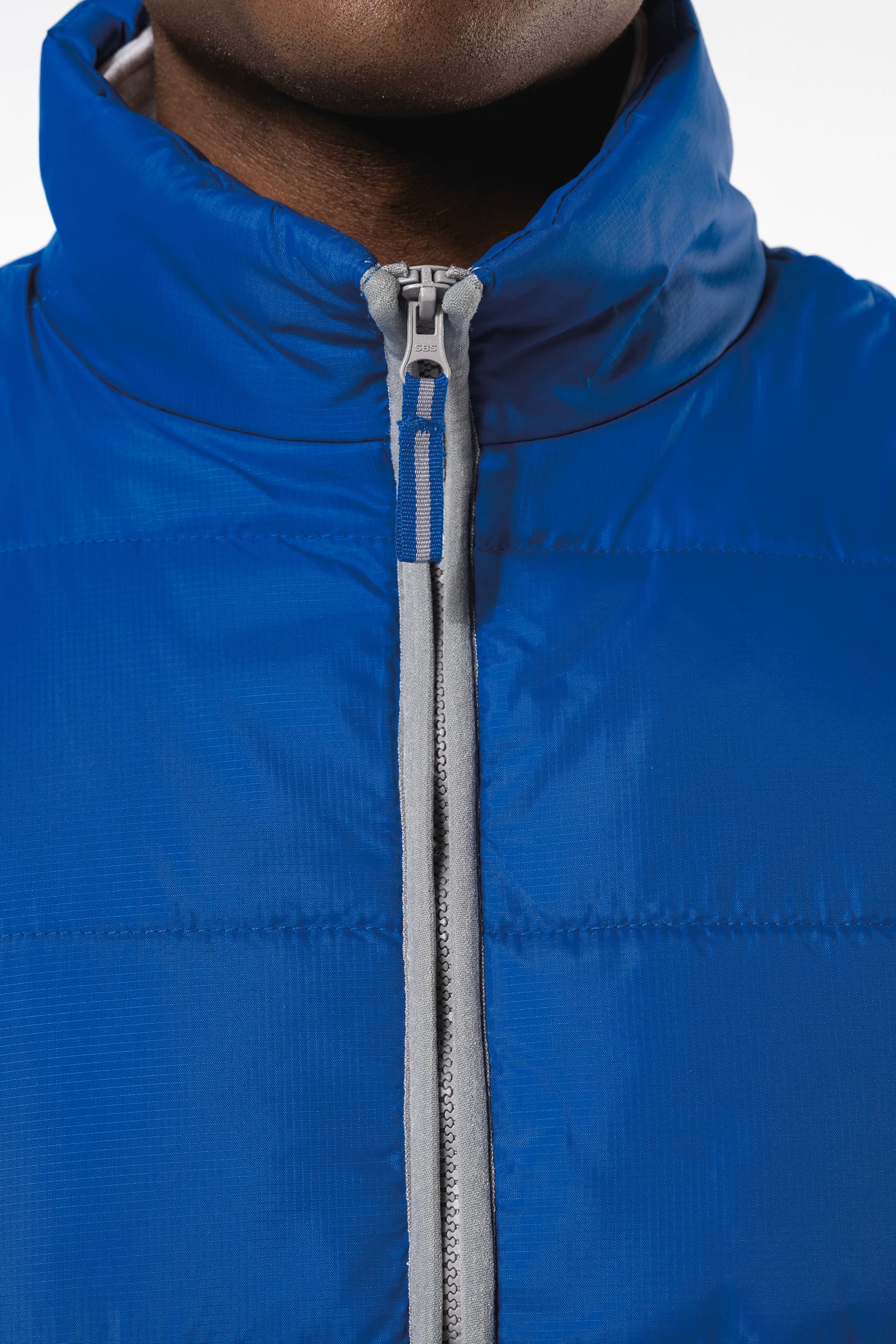 Jeune homme avec bonnet noir qui porte un bodywarmer matelassé bleu clair.