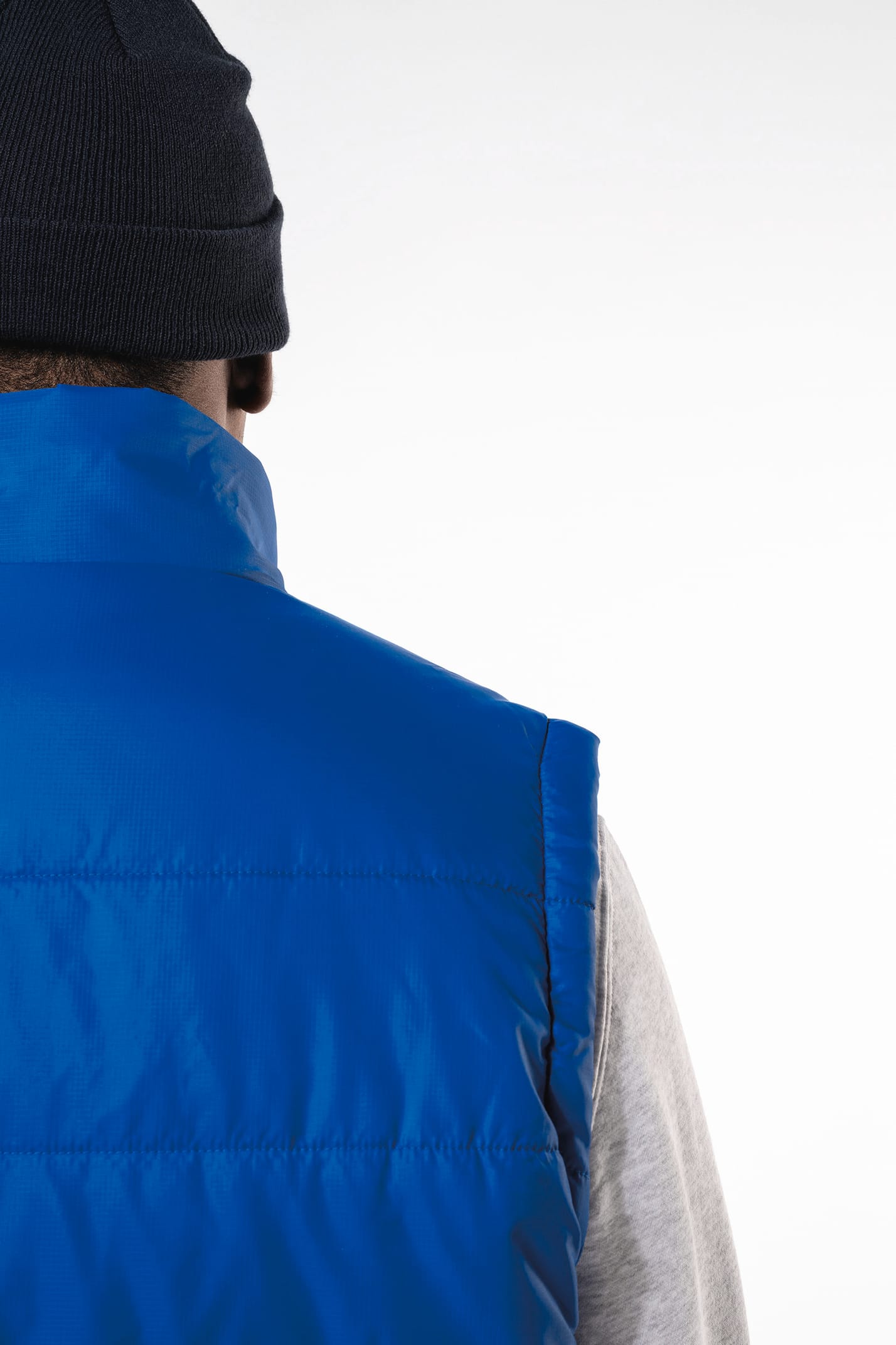 Jeune homme avec bonnet noir qui porte un bodywarmer matelassé bleu clair.