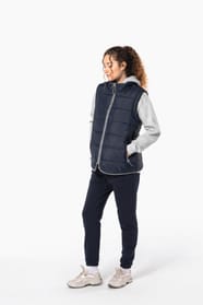 Jeune femme cheveux frisés attachés qui porte un bodywarmer matelassé bleu marine.