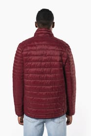 Jeune homme brun aux cheveux courts qui porte une doudoune légère bordeaux.