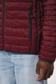 Jeune homme brun aux cheveux courts qui porte une doudoune légère bordeaux.