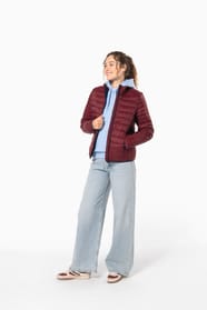 Jeune femme aux cheveux longs frisés attachés qui porte une doudoune légère bordeaux.