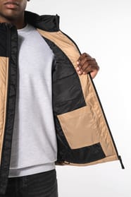 Jeune homme avec bonnet qui porte un bodywarmer matelassé bicolore beige et noir.