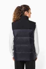 Jeune femme châtain frisée avec queue de cheval, qui porte un bodywarmer matelassé bicolore marine et noir.