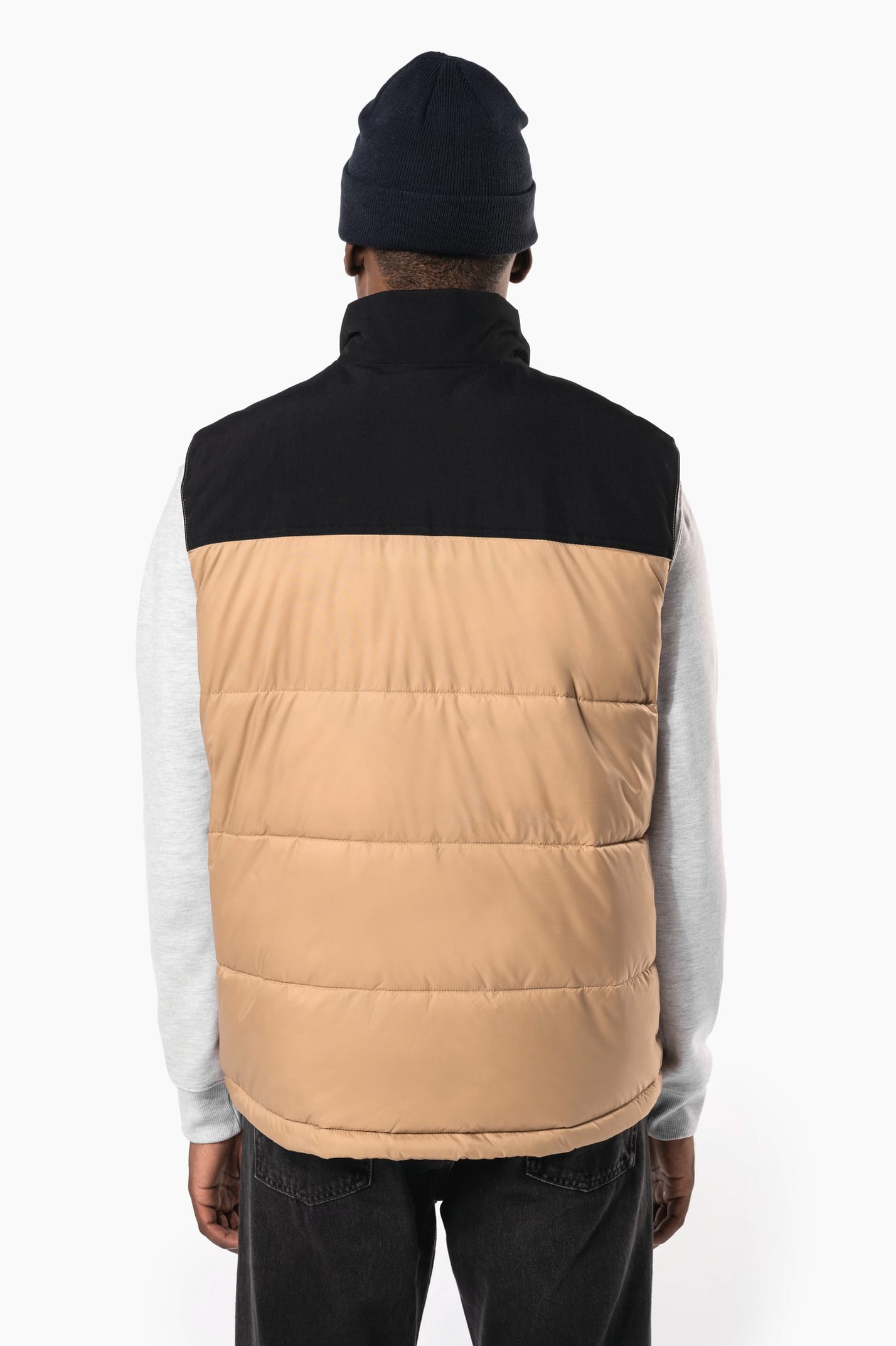 Jeune homme avec bonnet qui porte un bodywarmer matelassé bicolore beige et noir.