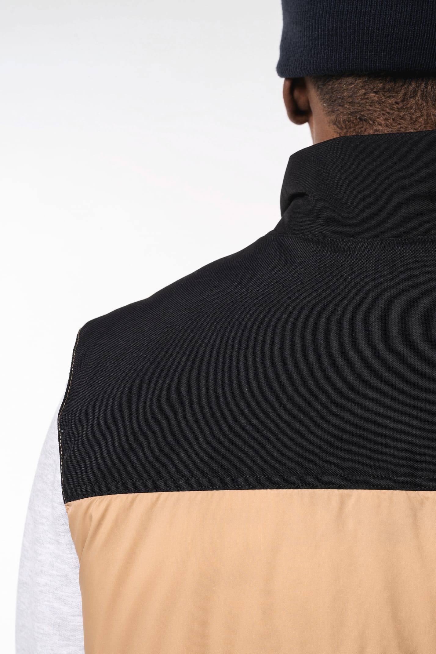 Jeune homme avec bonnet qui porte un bodywarmer matelassé bicolore beige et noir.