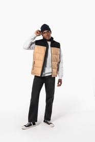 Jeune homme avec bonnet qui porte un bodywarmer matelassé bicolore beige et noir.