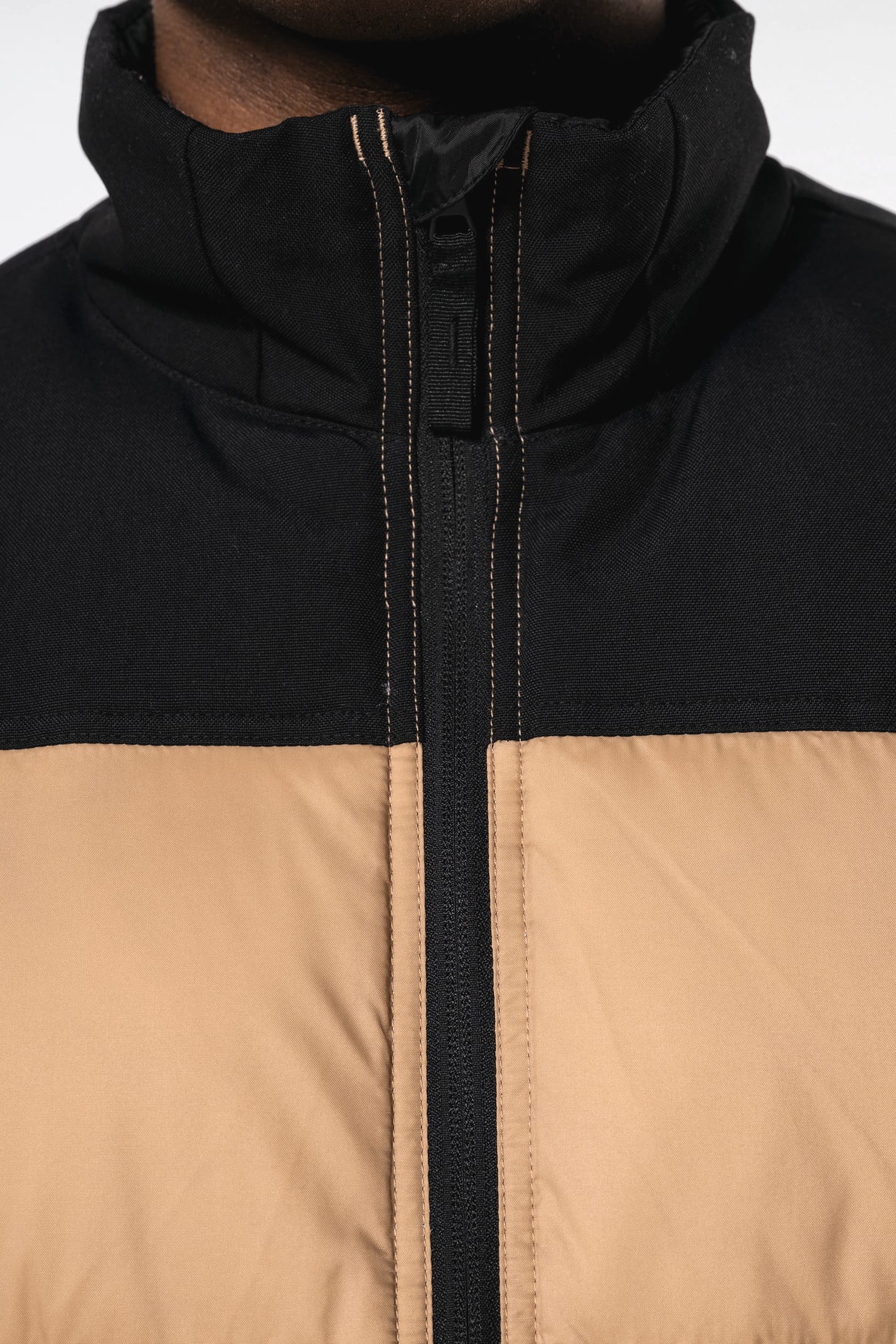 Jeune homme avec bonnet qui porte un bodywarmer matelassé bicolore beige et noir.