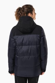Jeune femme châtain cheveux frisés attachés qui porte une parka matelassée à capuche bi-ton marine et noir.