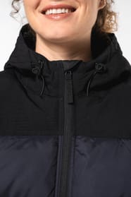 Jeune femme châtain cheveux frisés attachés qui porte une parka matelassée à capuche bi-ton marine et noir.
