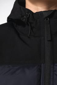 Jeune femme châtain cheveux frisés attachés qui porte une parka matelassée à capuche bi-ton marine et noir.