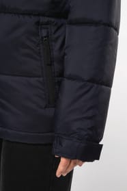 Jeune femme châtain cheveux frisés attachés qui porte une parka matelassée à capuche bi-ton marine et noir.