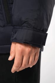 Jeune femme châtain cheveux frisés attachés qui porte une parka matelassée à capuche bi-ton marine et noir.