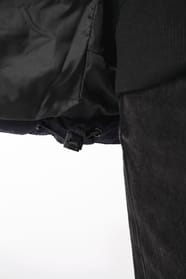Jeune femme châtain cheveux frisés attachés qui porte une parka matelassée à capuche bi-ton marine et noir.