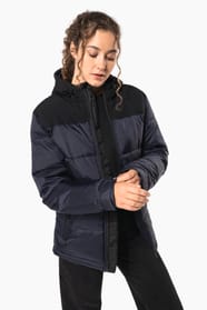 Jeune femme châtain cheveux frisés attachés qui porte une parka matelassée à capuche bi-ton marine et noir.