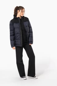 Jeune femme châtain cheveux frisés attachés qui porte une parka matelassée à capuche bi-ton marine et noir.