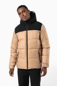 Jeune homme cheveux courts brun qui porte une parka matelassée à capuche bi-ton sable et noir.