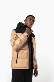 Jeune homme brun cheveux courts qui porte parka matelassée à capuche bi-ton sable et noire.