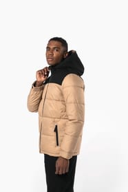 Jeune homme brun cheveux courts qui porte parka matelassée à capuche bi-ton sable et noire.