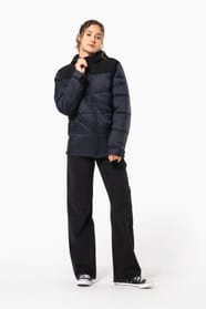 Jeune femme châtain cheveux frisés attachés qui porte une parka matelassée à capuche bi-ton marine et noir.