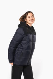 Jeune femme châtain cheveux frisés attachés qui porte une parka matelassée à capuche bi-ton marine et noir.