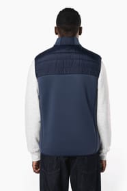 Jeune homme brun cheveux courts qui porte un bodywarmer bi matière bleu marine brillant.