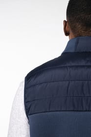 Jeune homme brun cheveux courts qui porte un bodywarmer bi matière bleu marine brillant.